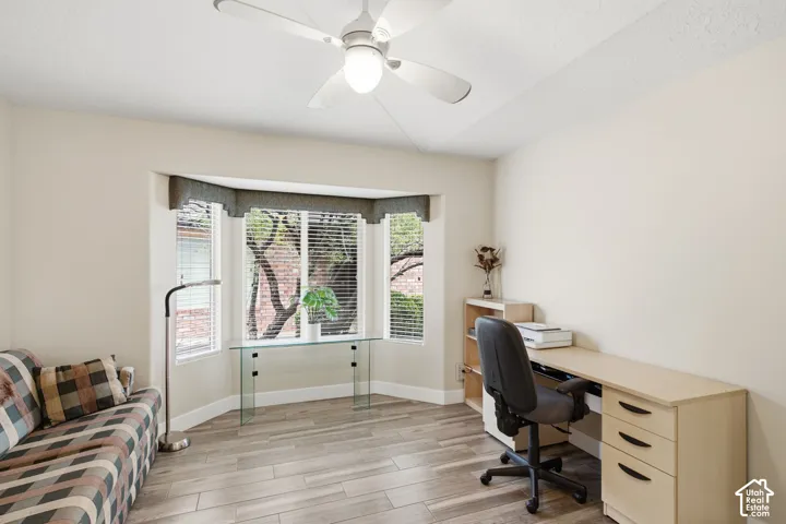 Bay window, ceiling fan with integrated lighting, and wood-finish flooring