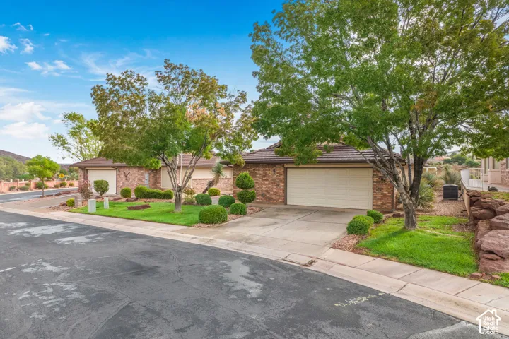 Single-story brick exterior featuring a multi-car garage, concrete driveway, tile roof, and landscaped grounds with stone retaining walls