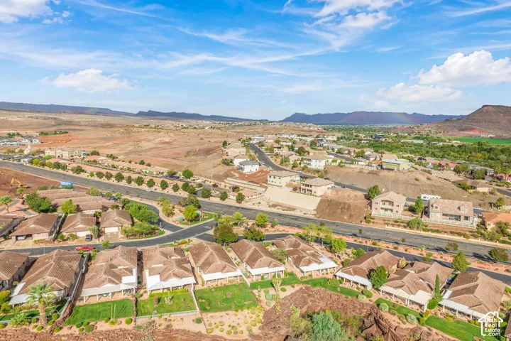 Aerial perspective of a residential neighborhood featuring paved streets, tile-roofed structures, manicured lawn areas, and prominent mountain backdrop