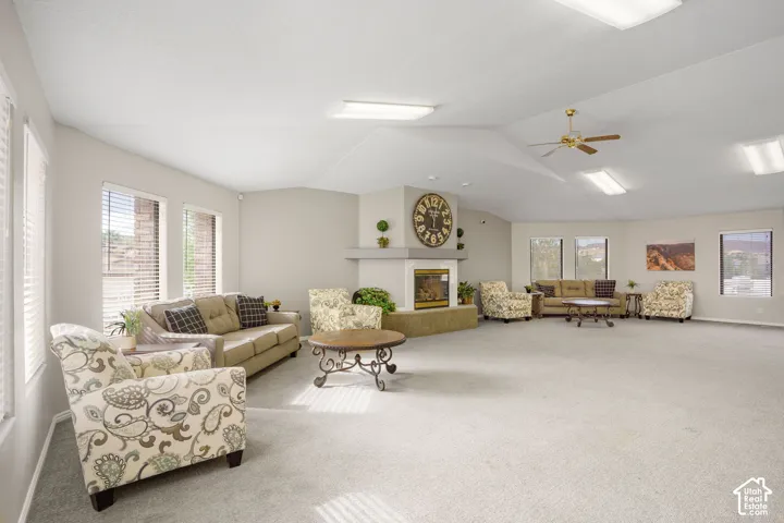Vaulted ceiling featuring recessed lighting and a central ceiling fan, anchored by a built-in fireplace with a raised masonry hearth and multiple large windows