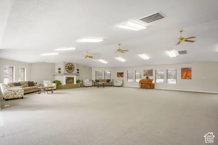 Expansive interior space featuring a vaulted ceiling, multiple ceiling fans, recessed fluorescent lighting, carpeting, and a fireplace with a stone-surround hearth