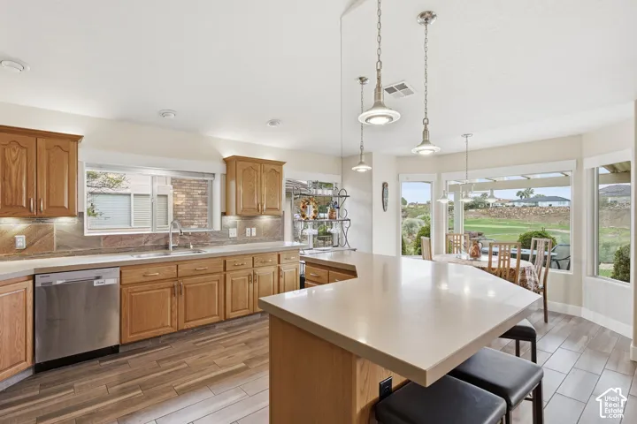 Kitchen featuring wood cabinetry, solid-surface countertops, wood-finish tile flooring, pendant lighting, and stainless steel dishwasher