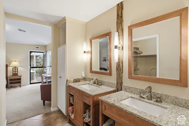 Dual vanity featuring light-toned stone countertops, undermount rectangular sinks, wooden cabinetry with open lower shelving, and matching wood-framed mirrors with vertical accent tile detailing