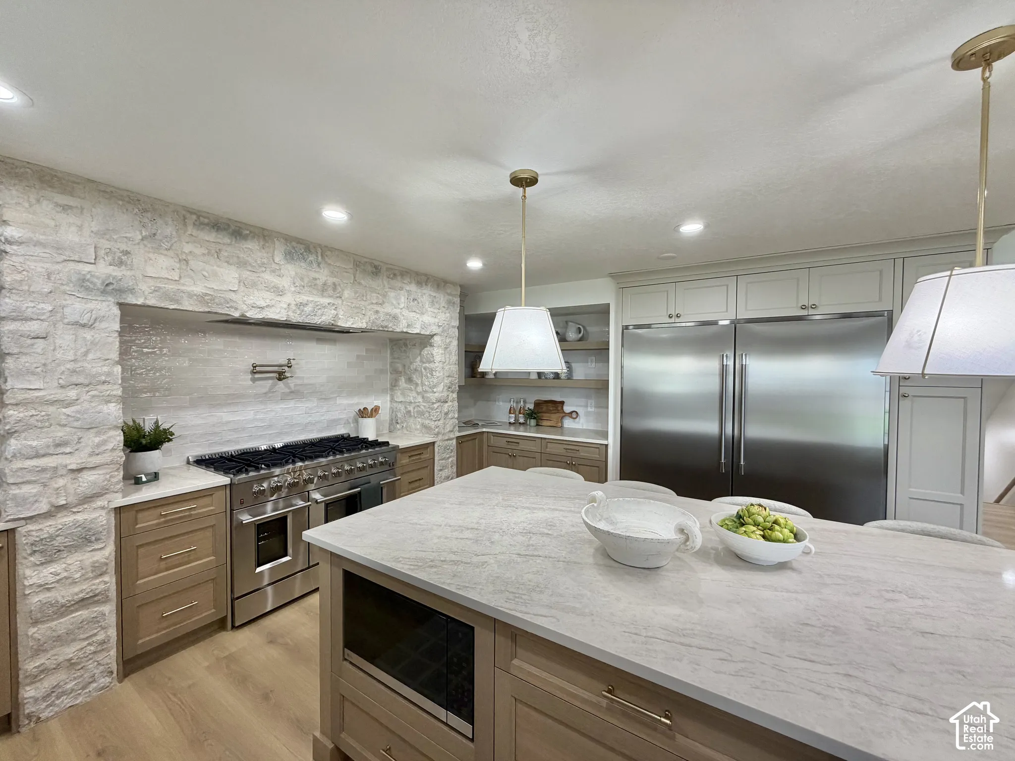 Kitchen featuring an oversized stone-clad cooking alcove, large center island with stone countertop, stainless steel dual-column refrigeration, recessed lighting, and wood-finish flooring