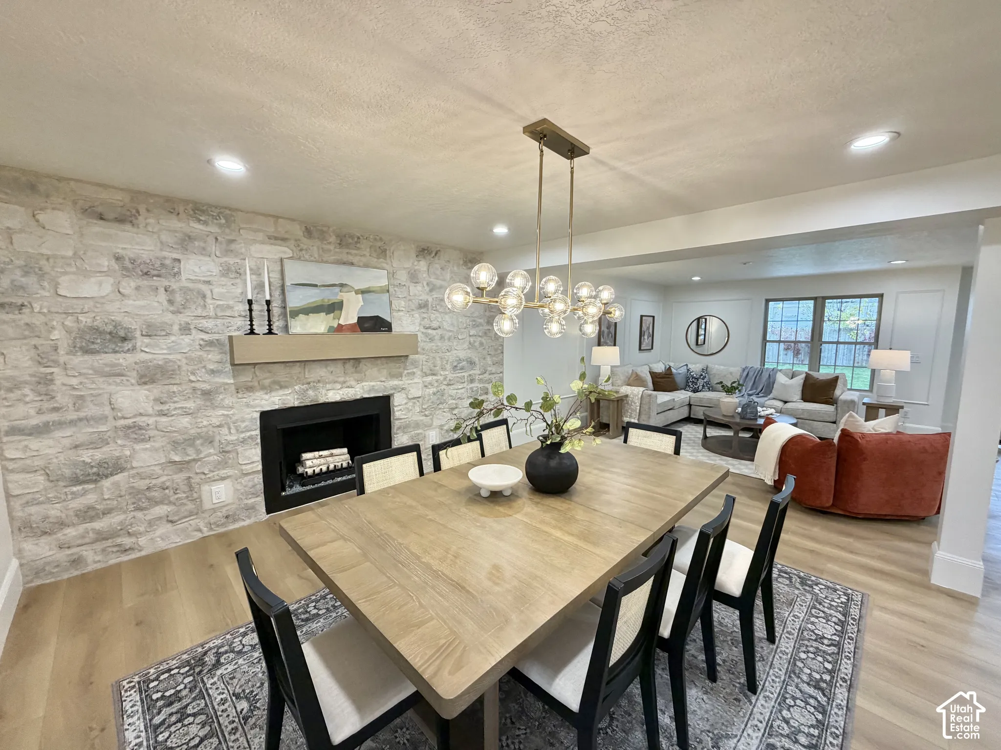 Floor-to-ceiling natural stone fireplace surround with integrated mantel, recessed lighting, wood-finish flooring, and multi-light chandelier