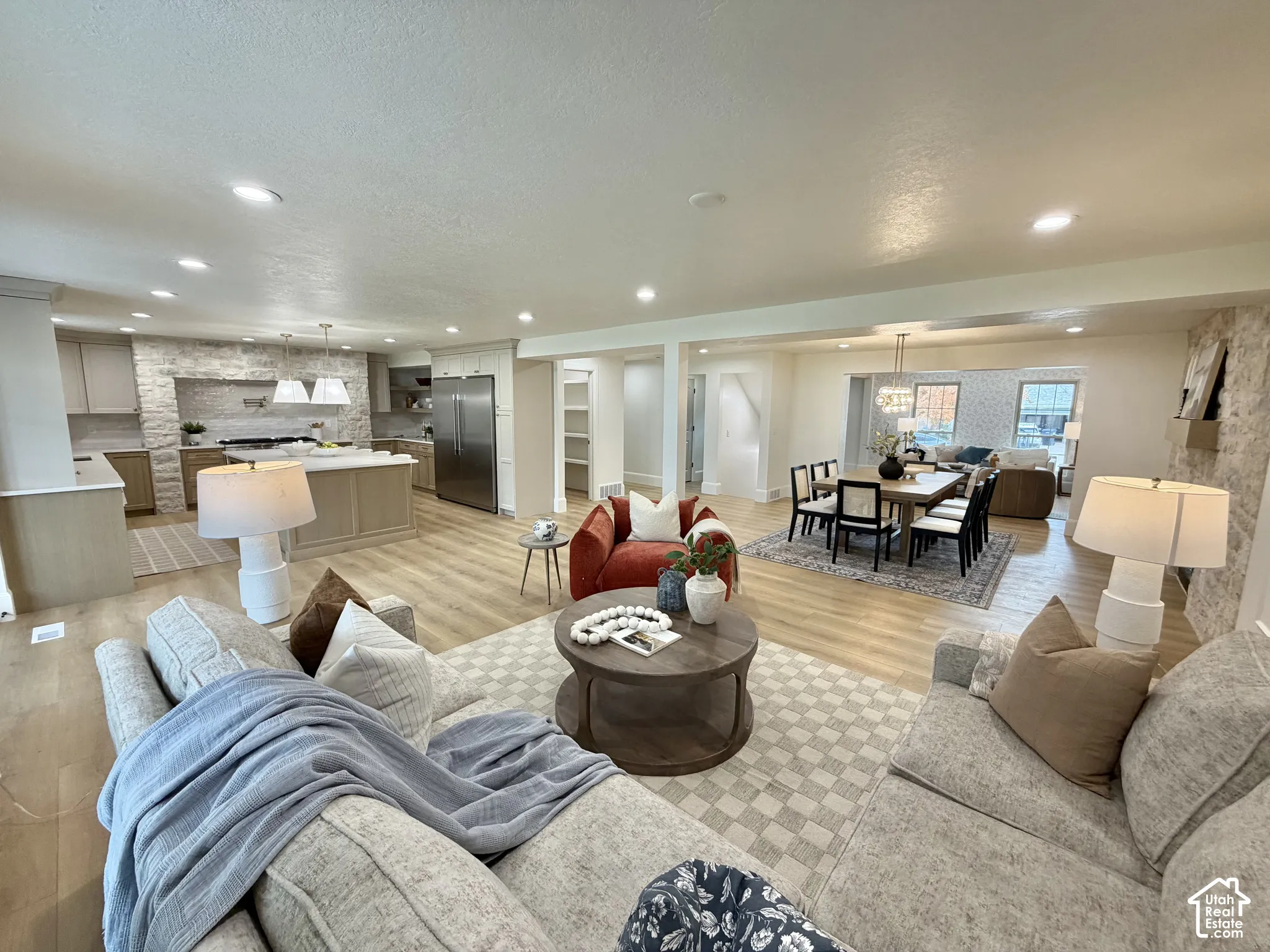 Open-concept living space featuring wood-finish flooring, recessed lighting, stone-accented walls, a kitchen island, and stainless steel appliances