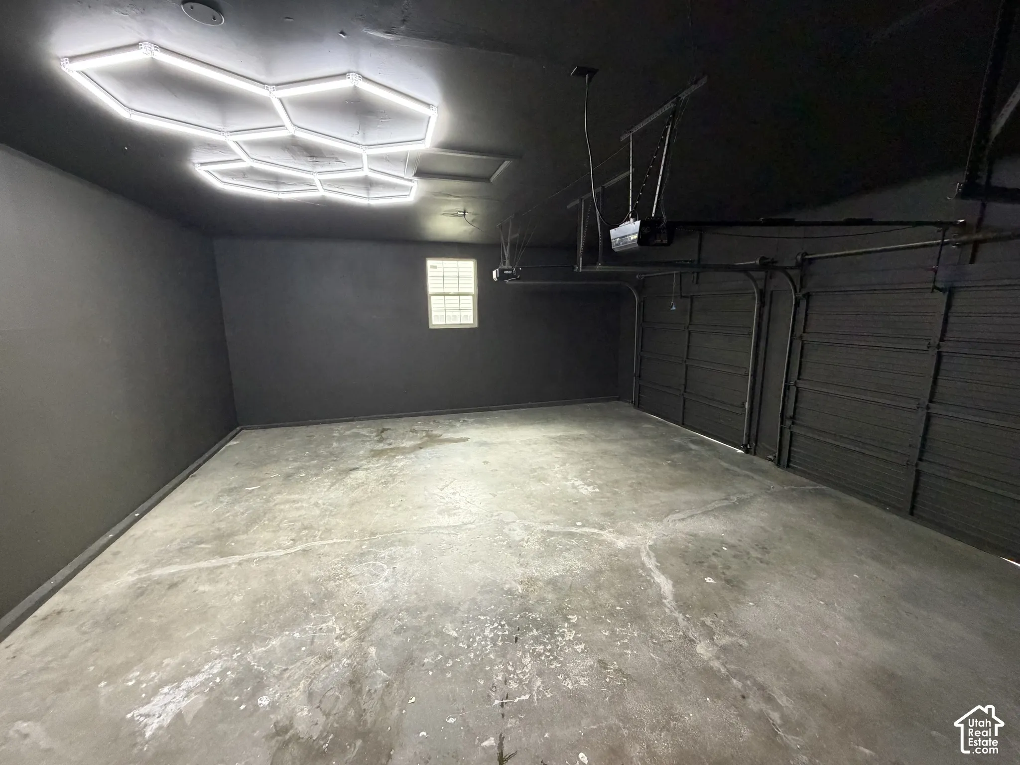 Garage space featuring matte black wall finishes, custom hexagonal geometric LED ceiling lighting, dual overhead garage door openers, and a concrete floor