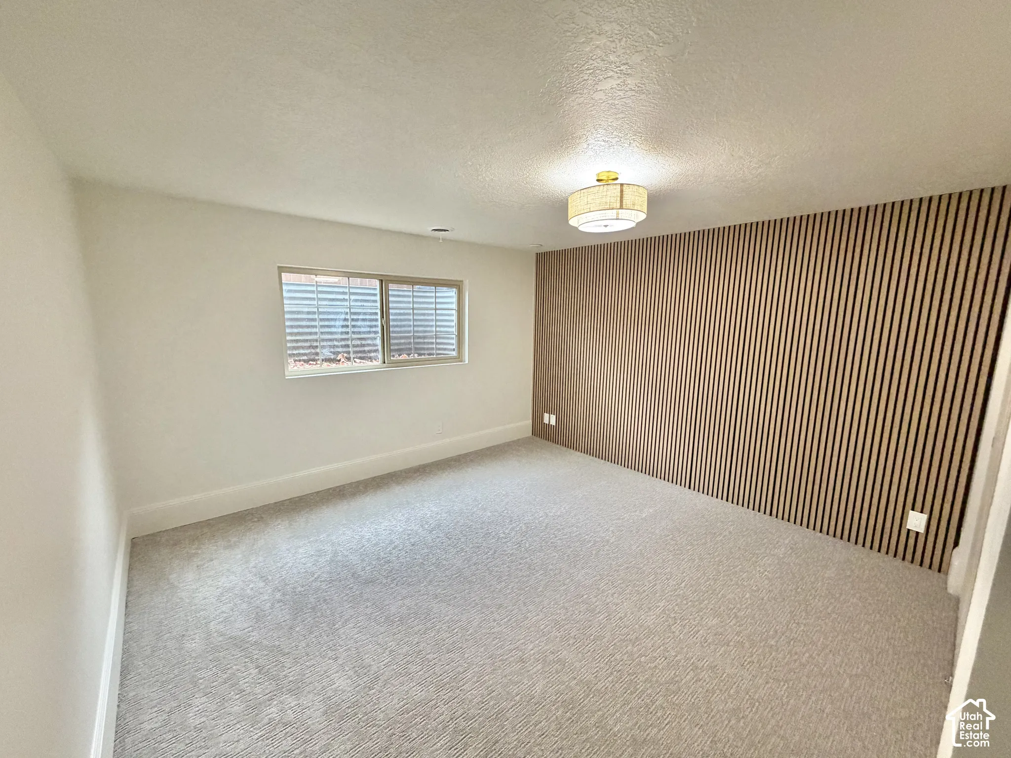 Neutral interior space featuring a floor-to-ceiling vertical slat wood accent wall, neutral carpeting, and a drum-style ceiling light fixture