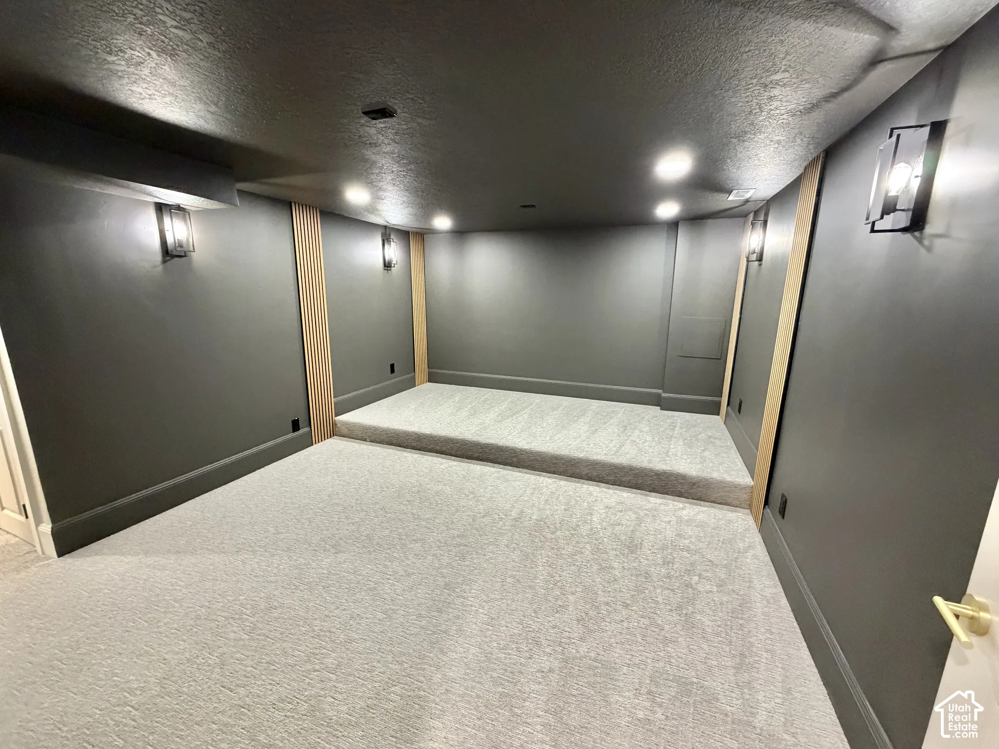 Room featuring a raised platform, recessed lighting, wall-mounted light fixtures, vertical wood-slat accent detailing, and wall-to-wall carpeting