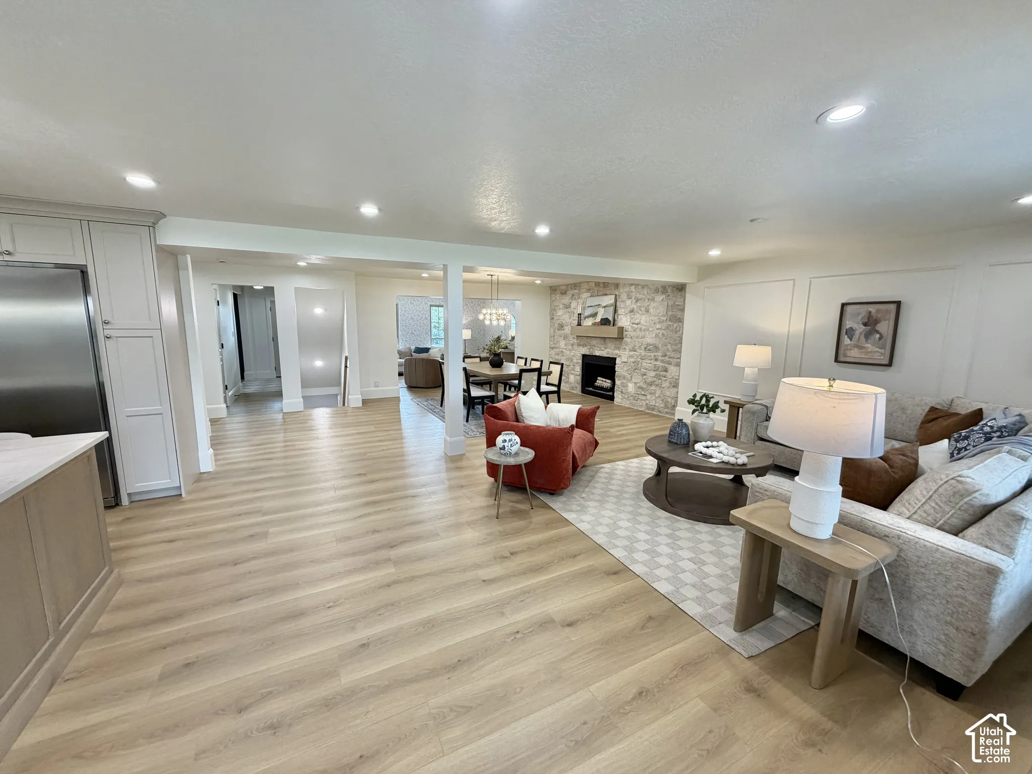 Open-concept interior featuring light wood-finish flooring, recessed lighting, a stone-surround fireplace with a floating mantel, and decorative wall paneling