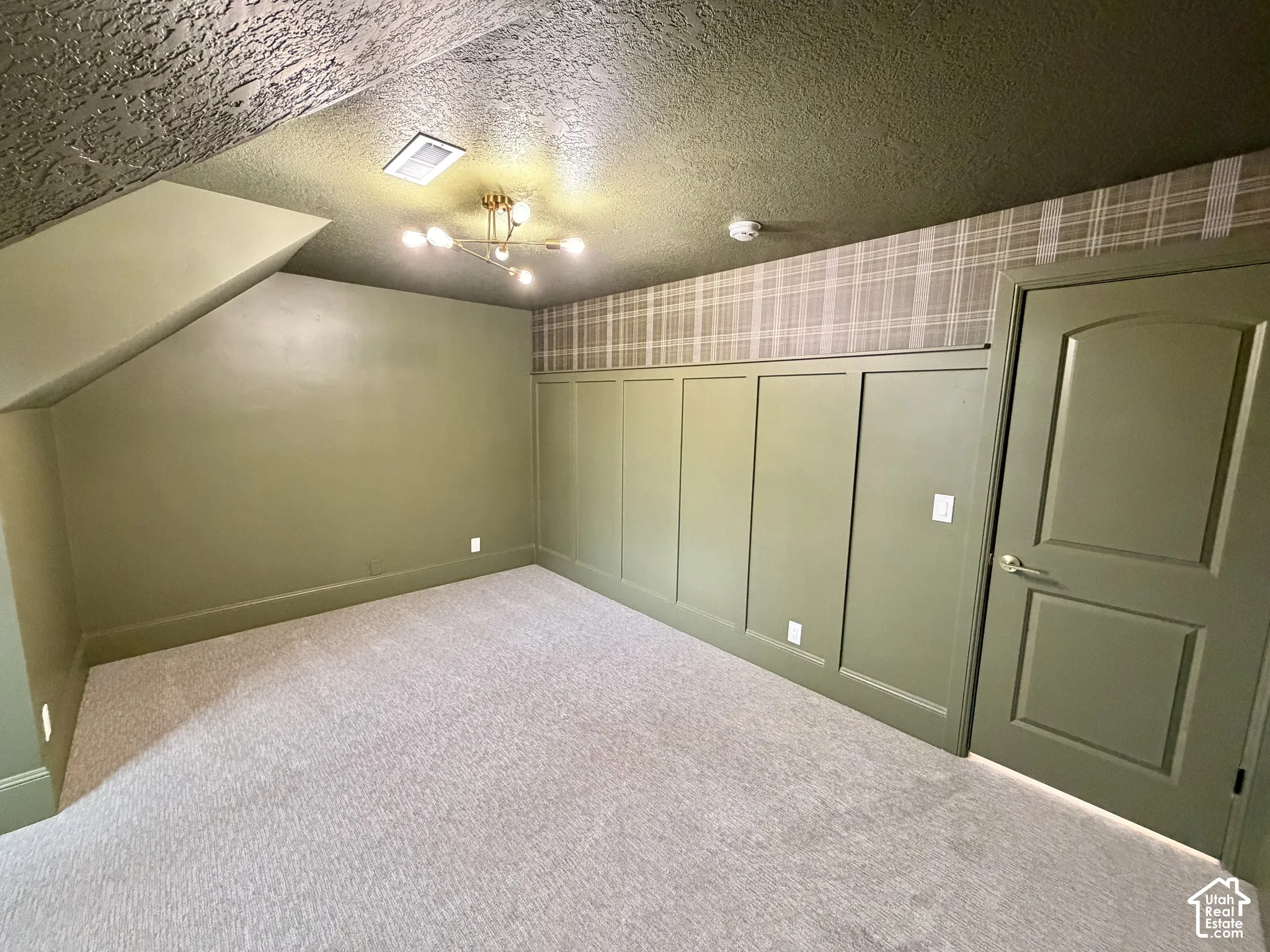 Interior room featuring wall-to-wall carpeting, wood paneling with decorative molding, plaid wallpaper accent, and a multi-arm modern light fixture