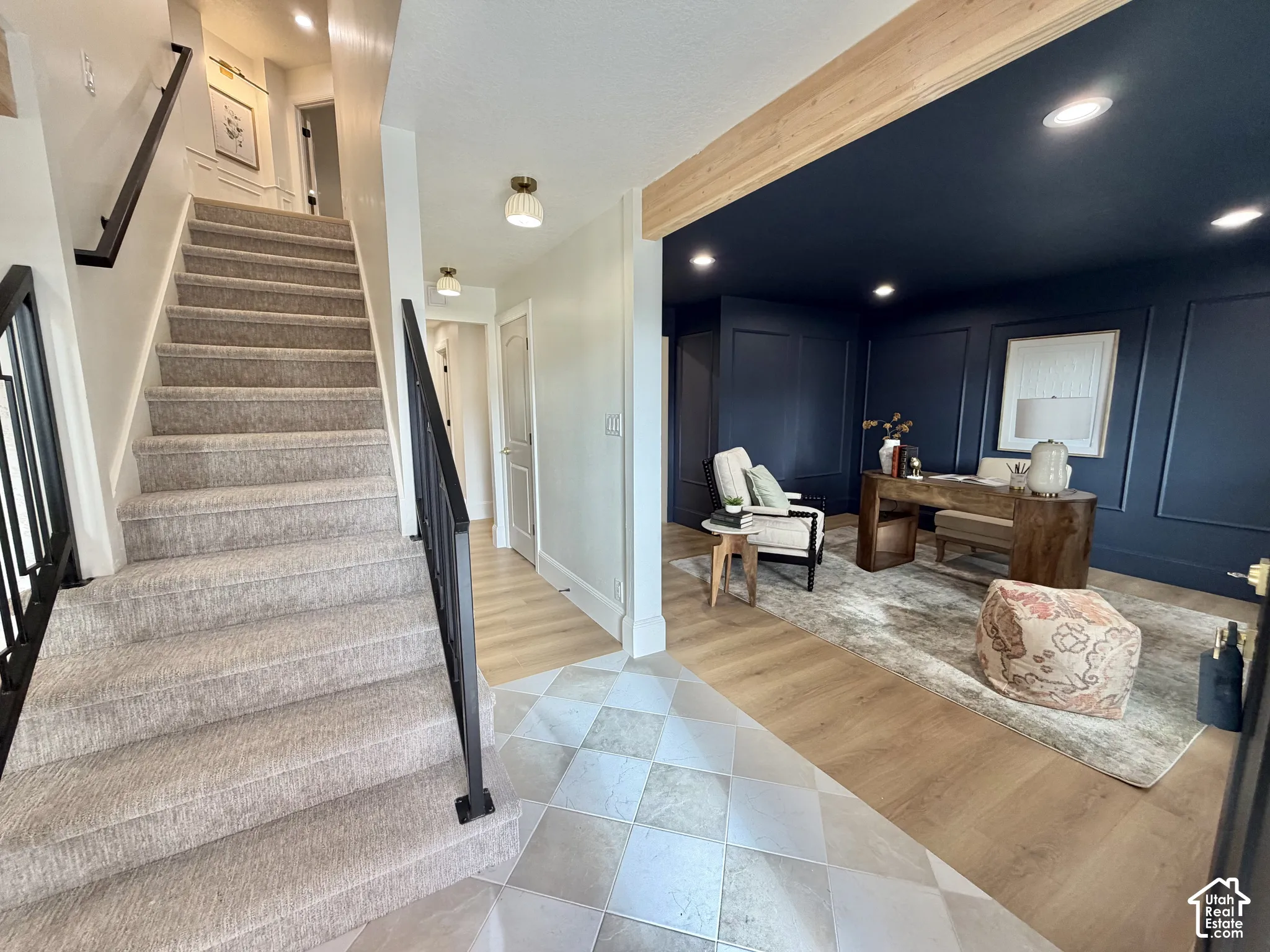 Entryway featuring a carpeted staircase with a matte black metal railing, patterned tile flooring, wood-finish flooring, and a room accented by dark-toned wainscoting and a natural wood ceiling beam