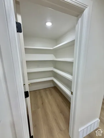 Walk-in storage space featuring wood-finish flooring, white built-in shelving, and recessed lighting