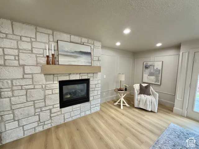 Floor-to-ceiling stone fireplace surround, natural wood mantel, wood-finish flooring, recessed lighting, and wall wainscoting