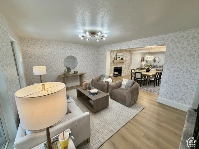 Living area featuring wood-finish flooring, patterned wallpaper, a multi-bulb geometric light fixture, and a stone-faced fireplace with a wood mantel