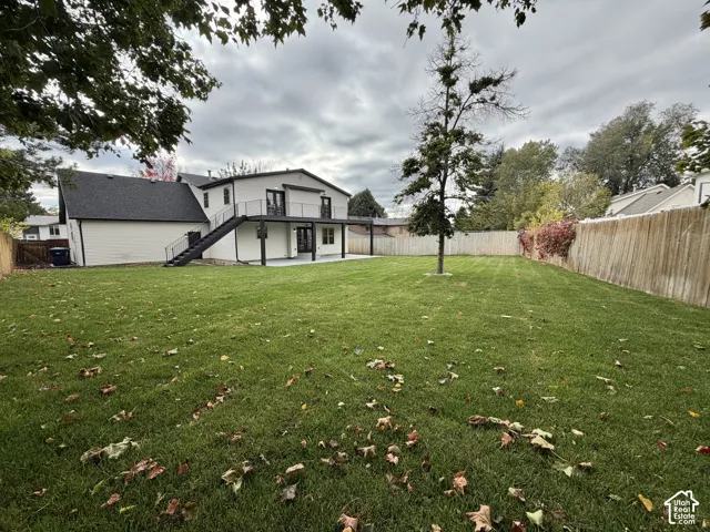 Expansive backyard featuring a level lawn, fenced perimeter, elevated metal deck with staircase, and a concrete patio