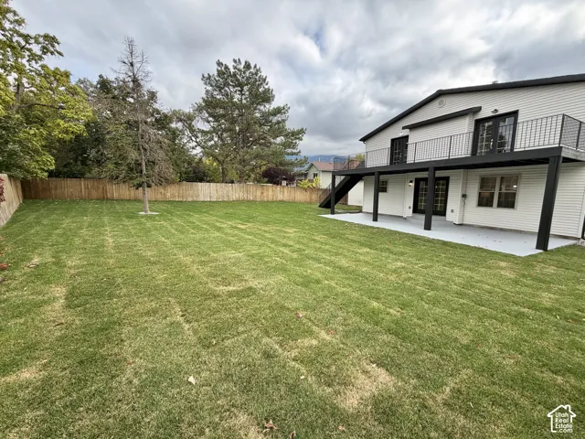 Expansive backyard featuring a level grass lawn, wood privacy fencing, a ground-level concrete patio, and a metal-railed upper deck