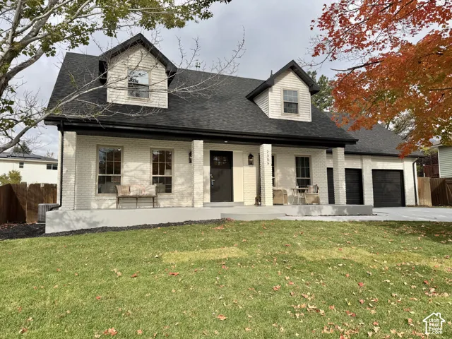 Exterior featuring a white brick facade, two upper-level dormer windows, a covered front porch, and an attached multi-car garage