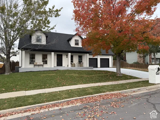Painted brick exterior featuring a covered front porch, dual dormer windows, asphalt shingle roof, and a two-car garage