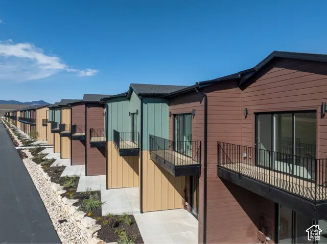 Multi-story exterior featuring multi-toned horizontal lap and vertical board-and-batten siding, private elevated balconies with black metal railings, and concrete ground-level patios