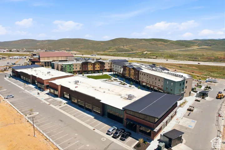 Mixed-use complex featuring multi-story masonry and metal-clad structures, expansive surface parking, central grass courtyard, and mountain backdrop