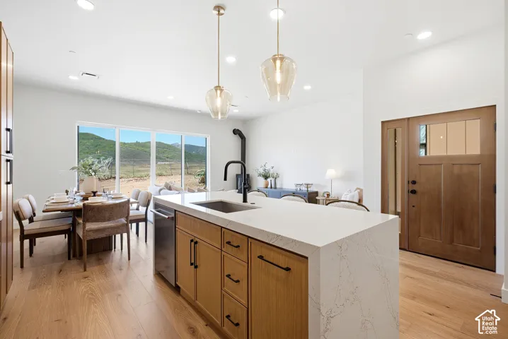 Kitchen featuring a waterfall-edge quartz island, wood-finish cabinetry, recessed lighting, and wood-finish flooring, complemented by a wooden entry door with an integrated window