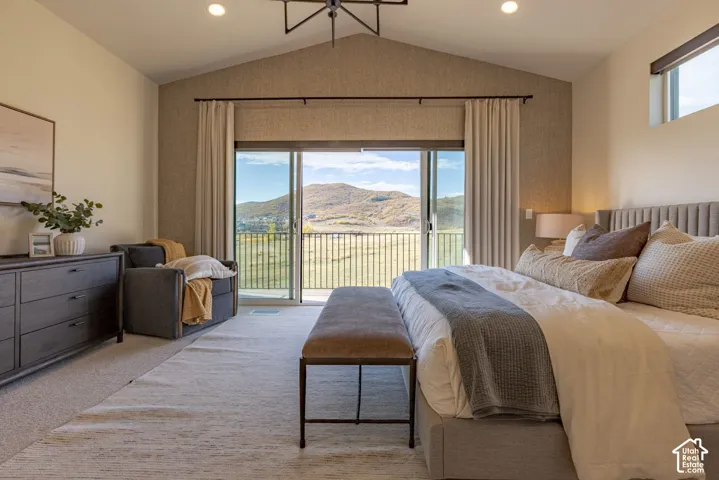 Vaulted ceiling with a geometric chandelier, textured accent wall, sliding glass doors opening to a balcony with metal railing, and expansive mountain scenery