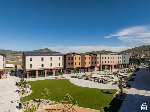 Multi-story exterior featuring a mix of brick and siding finishes, expansive courtyard with synthetic turf, curved stone-masonry retaining walls, hardscaped walkways, and a mountain backdrop