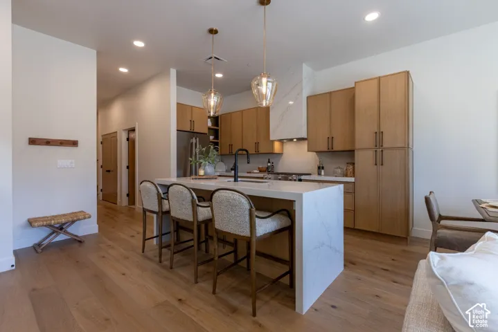 Kitchen featuring flat-panel wood cabinetry, a waterfall island with a white stone-finish countertop, dual glass pendant lights, and wood-finish flooring