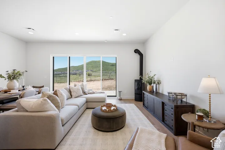 Open floor plan with wood-finish flooring, floor-to-ceiling sliding glass doors, mountain scenery, and a matte black freestanding wood-burning stove