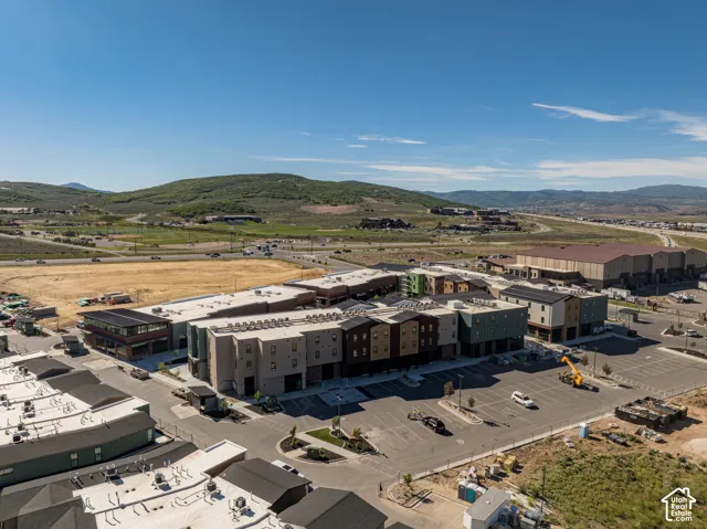 Multi-story commercial complex featuring industrial-inspired architecture, mixed-material exterior siding, flat roofing, expansive surface parking, and a backdrop of mountain terrain