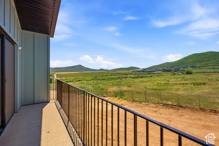 Covered balcony with a metal railing, featuring expansive mountain and open space scenery