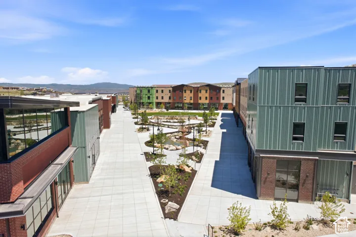 Mixed-use complex featuring industrial-style metal siding, red brick masonry, concrete pedestrian pathways, integrated landscaping, and mountain backdrop