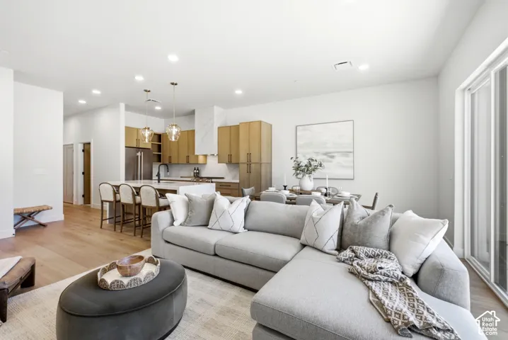 Open-concept living space featuring wood-finish flooring, recessed lighting, a central kitchen island with a dual-tone finish, floor-to-ceiling cabinetry, and sliding glass doors