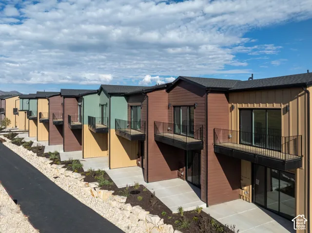 Multi-unit exterior featuring mixed-material siding in earth tones, private elevated balconies with metal railings, sliding glass doors, and concrete patios