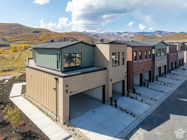 Multi-level exterior featuring a combination of brick and vertical metal siding, attached garage, concrete driveway, and mountain backdrop