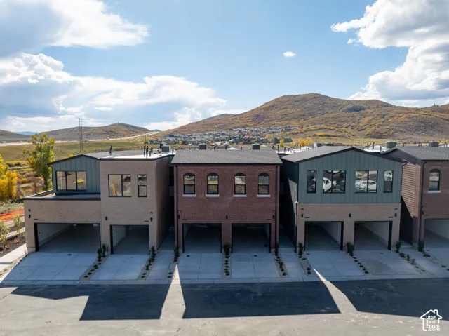 Multi-unit exterior featuring mixed brick and vertical siding facades, arched window detailing, integrated garage bays, and mountain backdrop