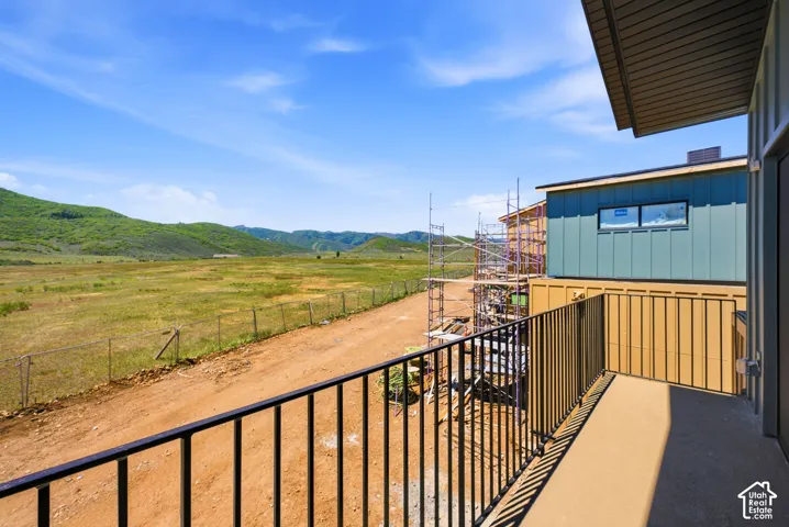 Covered balcony with black metal railing, vertical panel siding, and mountainous terrain