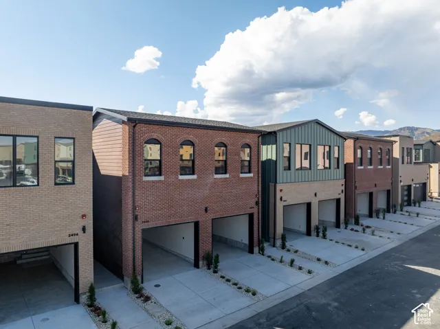 Multi-story residential exterior featuring brick and metal siding, arched window detailing, integrated garages, and concrete driveways