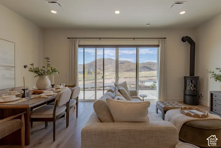 Open-concept living space featuring wood-finish flooring, recessed lighting, a modern black cylindrical wood-burning stove, and expansive sliding glass doors with mountain scenery