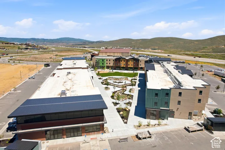 Aerial view of multi-building commercial property featuring flat roofs, dark metal awnings, multi-story brick and panel siding exteriors, paved courtyards, and a mountainous backdrop