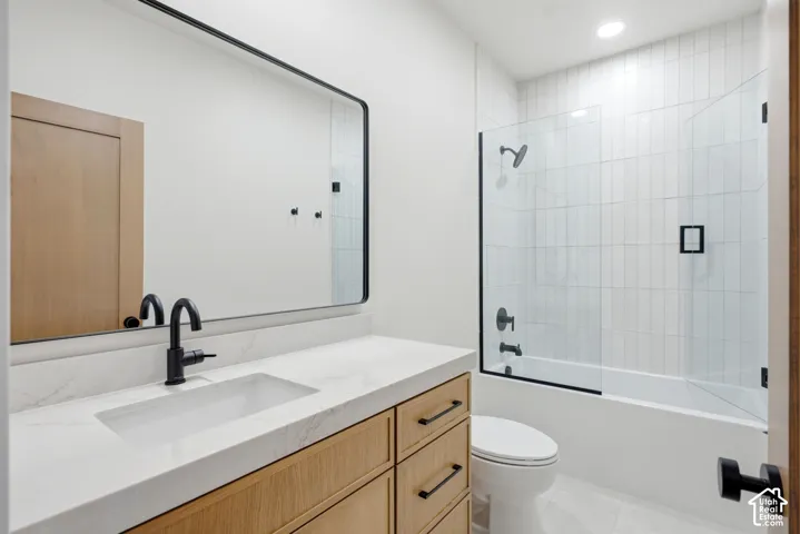 Bathroom featuring a light-finish wood vanity with a white countertop, an integrated sink, a rectangular mirror with a black frame, and a tub-shower combination with vertical tile surrounds and matte black hardware