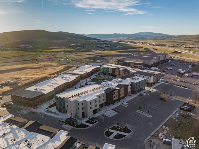 Aerial perspective of a multi-building complex featuring varied exterior siding, flat roofing, paved surface parking, and a central courtyard area against a mountain backdrop