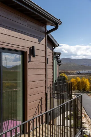Horizontal siding exterior featuring matte black metal railings, tall glass sliding doors, dark gutter systems, and minimalist wall-mounted outdoor lighting, set against a mountain backdrop