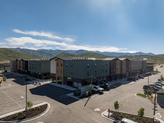Multi-story exterior featuring metal siding, brick facade, flat roofing, paved parking area, and mountain backdrop