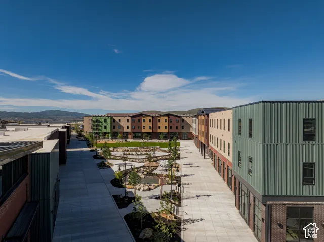 Multi-story exterior featuring ribbed metal siding, brick masonry, concrete walkways, and tiered landscaping with decorative stone elements