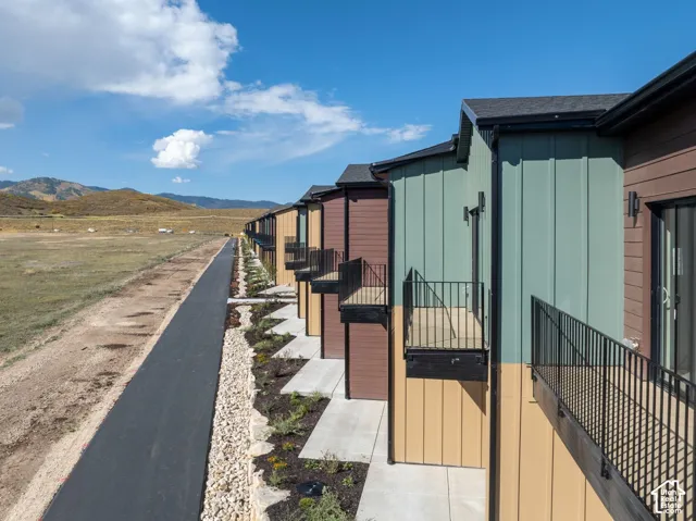 Multi-story exterior featuring vertical metal siding, horizontal lap siding, private iron-railed balconies, concrete patio walkways, and exterior wall-mounted lighting