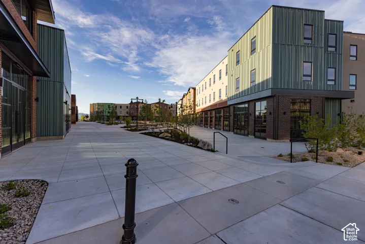Contemporary multi-story exterior featuring corrugated metal siding, dark brick masonry, floor-to-ceiling glass paneling, and concrete hardscaping