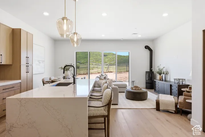 Kitchen island featuring a waterfall edge and quartz countertop, wood-finish flooring, recessed lighting, glass pendant fixtures, and a freestanding cylindrical stove