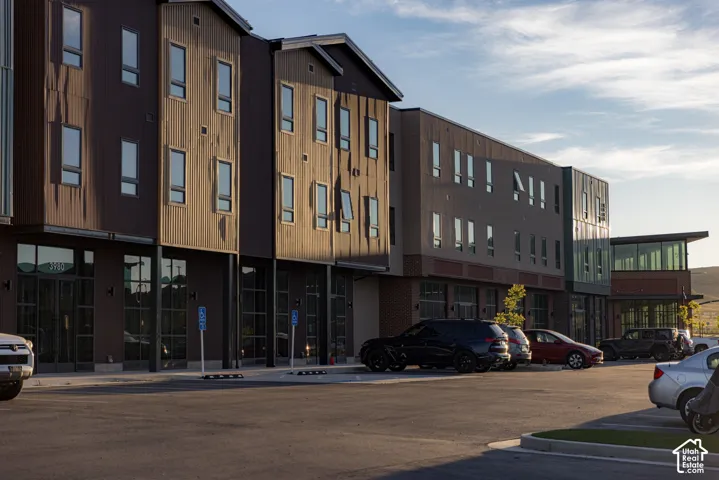 Multi-story building exterior featuring vertical metal and masonry siding, expansive glass storefronts, and a paved parking area